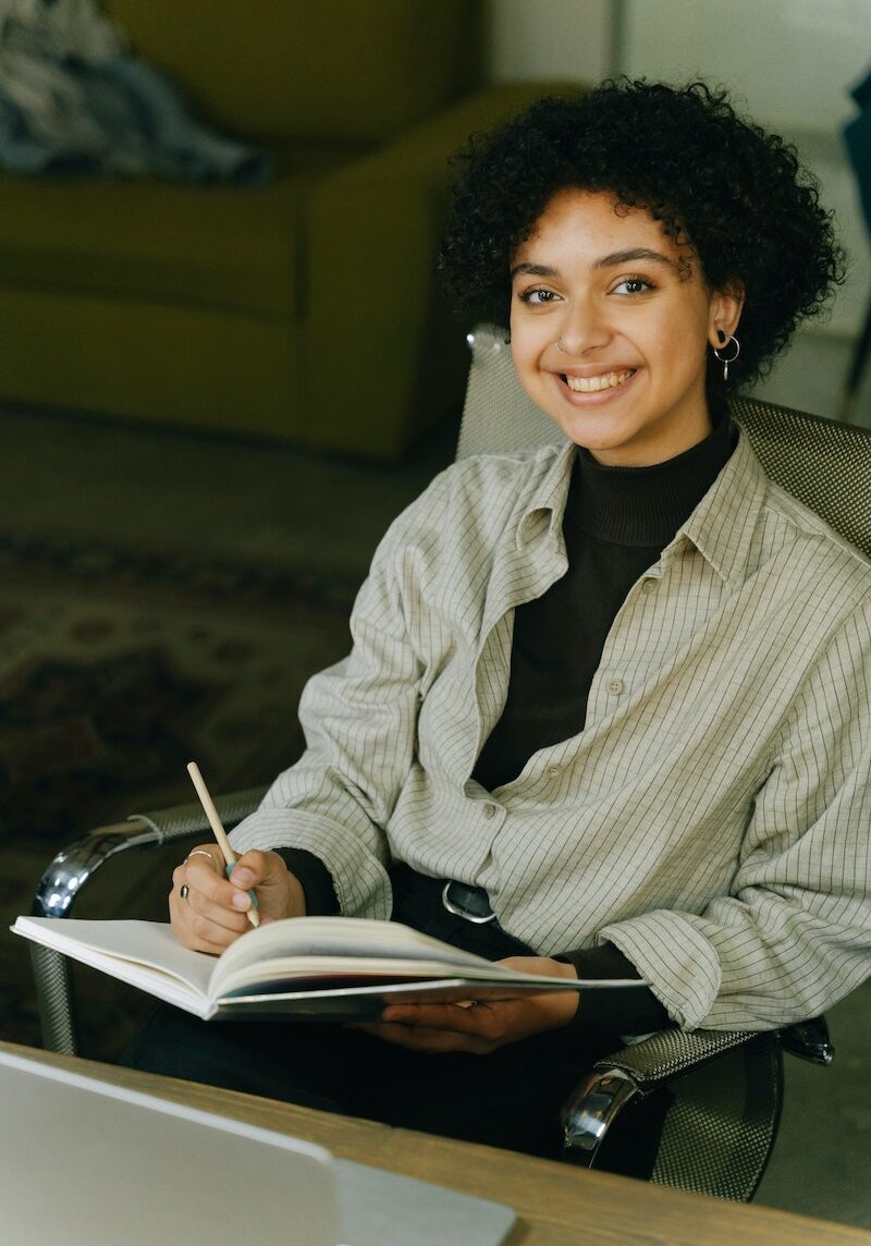 A Woman Sitting on the Chair while Holding a Pen and Notebook